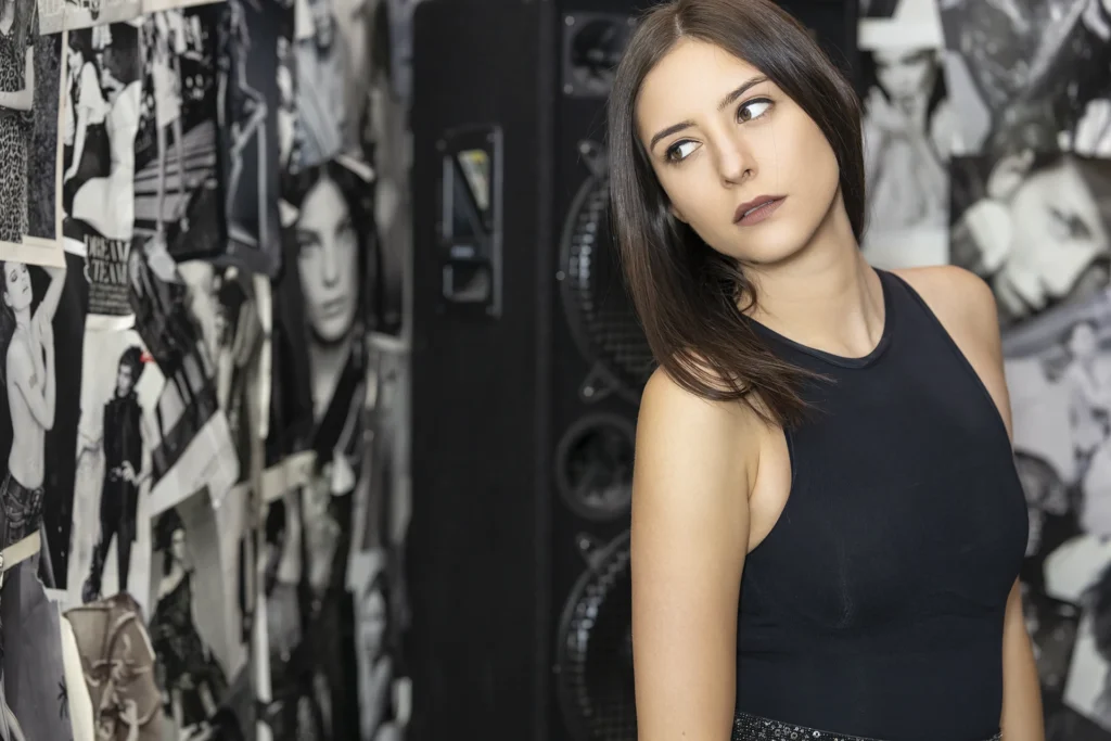 Frau mit dunklem Top blickt ernsthaft zur Seite, im Hintergrund Schwarz-Weiss-Collagen