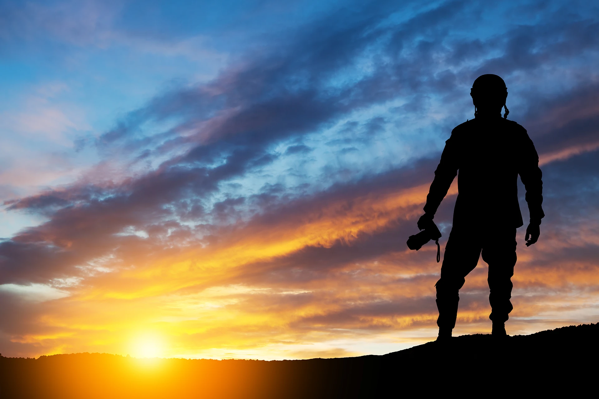 Silhouette eines Fotografen mit Kamera im Gegenlicht bei Sonnenuntergang vor dramatischem, farbintensivem Himmel